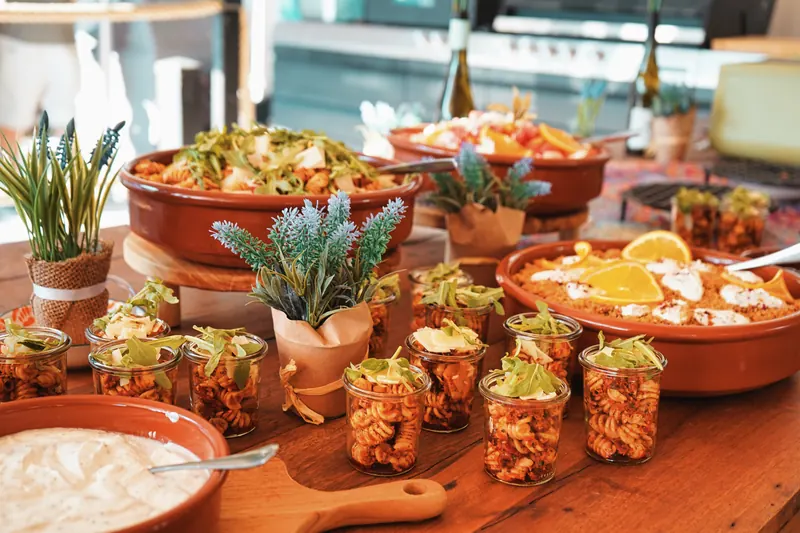 Buffet mit Pastasalat im Glas, Couscous und Dips in Terrakotta-Schalen