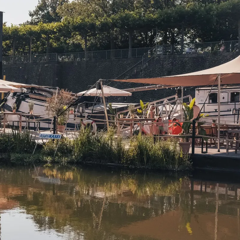 Der Harbor Club vom Wasser aus gesehen mit Sonnensegeln und Pflanzen