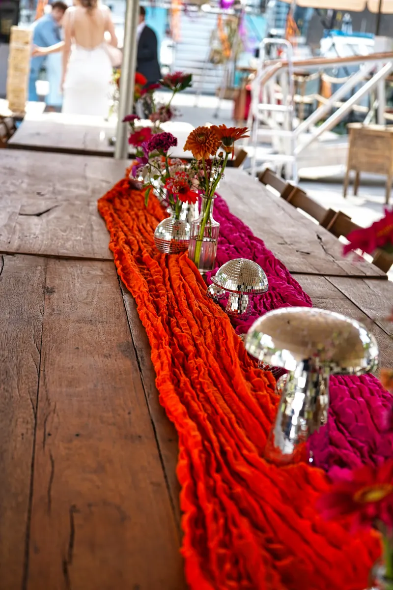 Hochzeitstafel mit orangefarbenem Tischläufer, Blumen und Discokugel-Pilzen