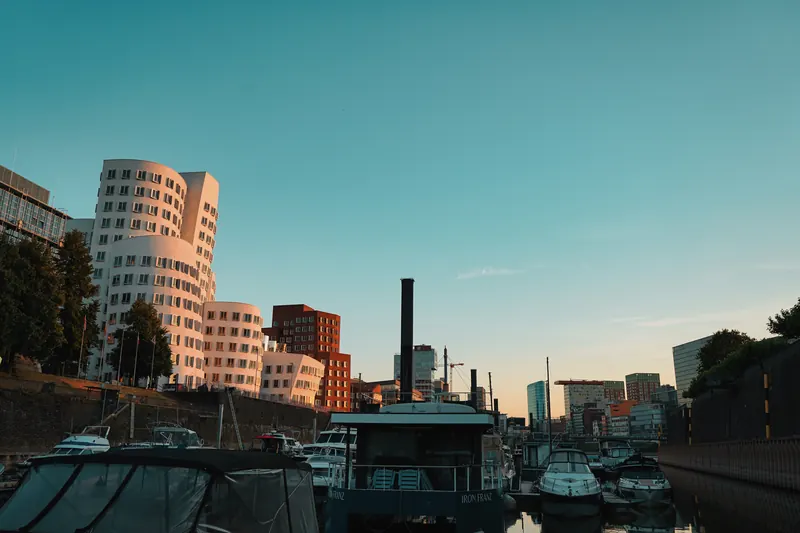 Gehry-Bauten im Medienhafen bei Sonnenuntergang, davor Boote in der Marina