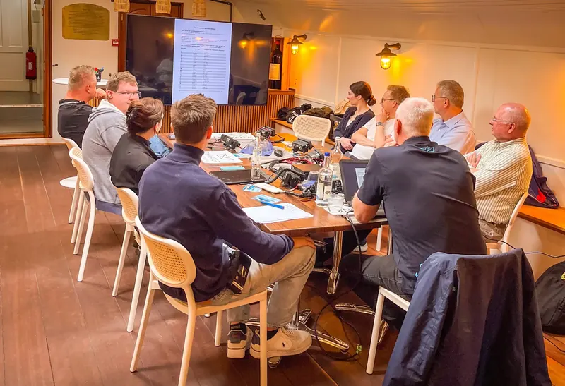 Team-Meeting an einem langen Tisch im Innenraum des Harbor Club