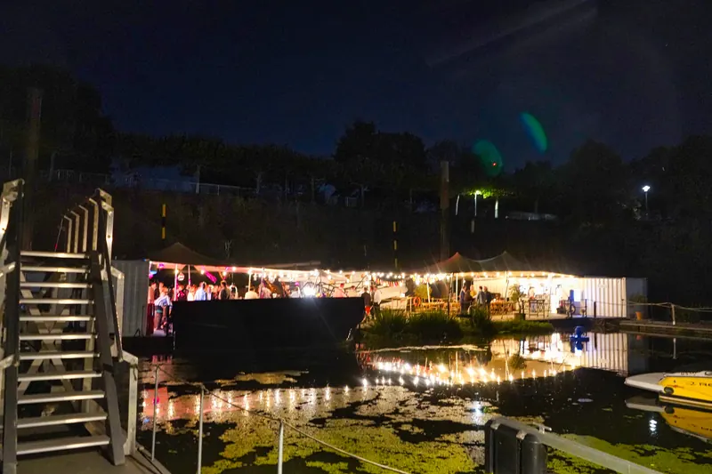 Der beleuchtete Harbor Club bei Nacht, die Lichter spiegeln sich im Wasser