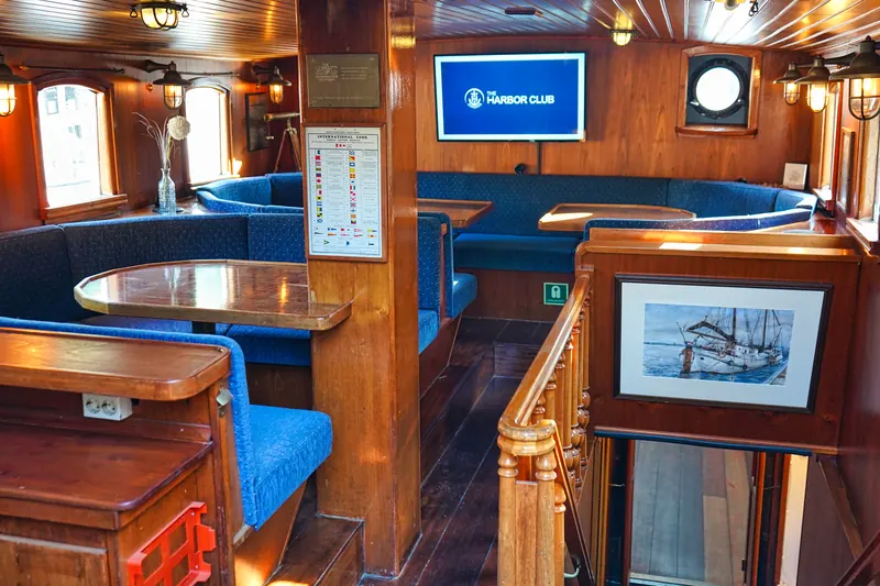 Salon an Bord mit blauen Sitzbänken, Holzvertäfelung und Bildschirm mit Harbor-Club-Logo
